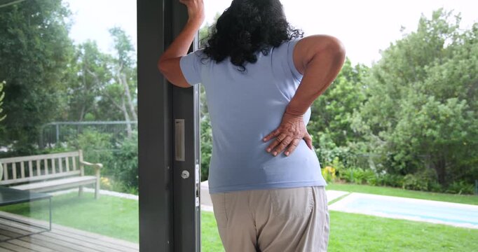Senior African American woman entering doorway, feeling sharp back pain, rubbing back moving inside