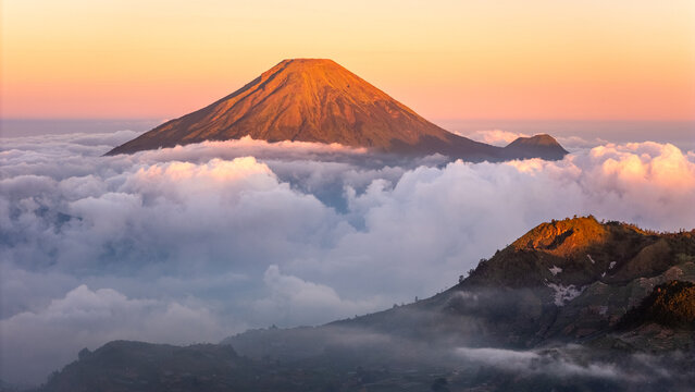 Aerial view of Mount Sindoro peak rising above a thick sea of clouds during golden hour in Indonesia.