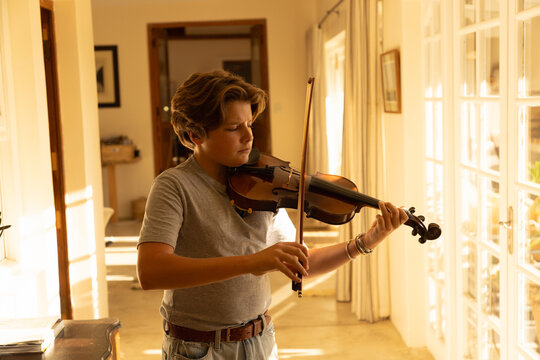 pre teen boy playing violin indoors at sunset