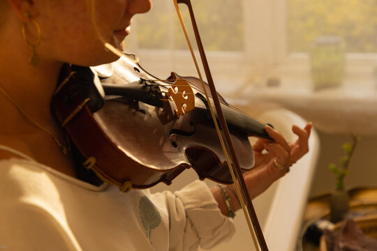 portrait of young woman playing violin in bathroom at sunset