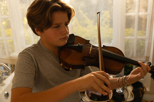 pre teen boy playing violin indoors at sunset