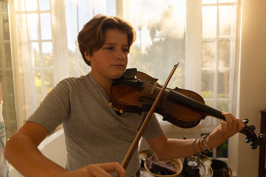pre teen boy playing violin indoors at sunset