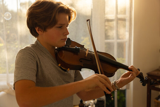 pre teen boy playing violin indoors at sunset