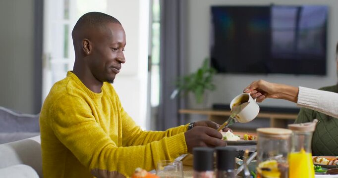 African American couple at table woman pouring from pitcher flavoring his food man guiding laughing