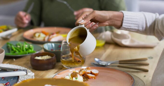 White gravy jug is tilting, pouring brown gravy onto terracotta plate at table to coat meat