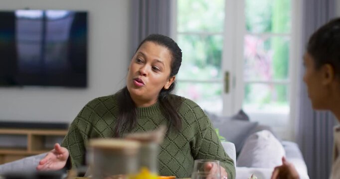 African American women chatting at dining table during meal, gesturing laughing and catching up