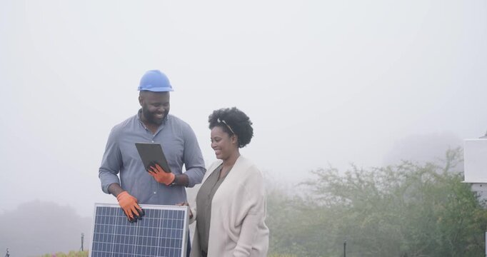 After client pointing at roof African tech consulting tablet while holding solar panel for setup