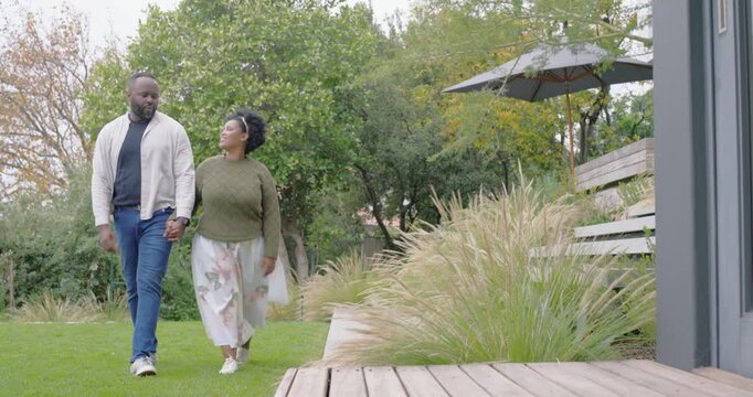 African couple starting backyard stroll, holding hands and walking toward wooden deck, talking