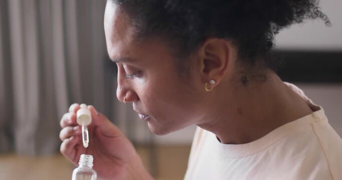 Adult African man looking down, opening dropper, drawing liquid, inhaling scent to inspect at home