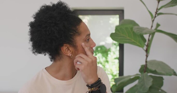 African American male inspecting spot, holding white applicator rubbing right cheek by potted plant