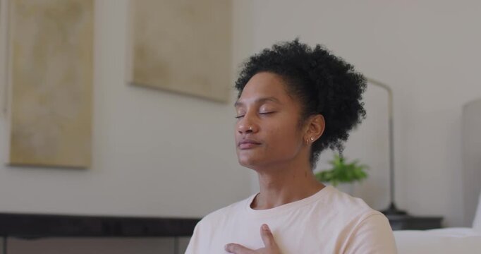 African American adult woman closing eyes calming on sofa placing right hand on chest showing watch
