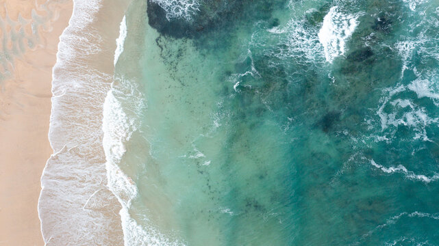 Aerial view of turquoise ocean waves crashing onto the sandy shore of Constantine Bay in Padstow, Cornwall, United Kingdom.