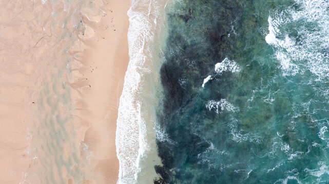 Aerial view of the sandy shoreline of Constantine Bay with turquoise ocean water and gentle waves breaking on the beach in Padstow, Cornwall, United Kingdom.