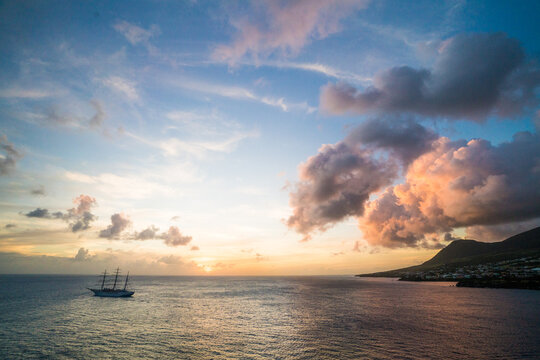 Tall ship sails along a coastal town at sunset