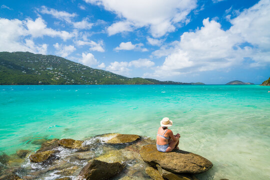 Woman in a hat looks out at a turquoise sea