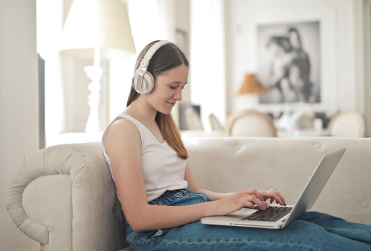 Young woman with headphones using laptop on sofa