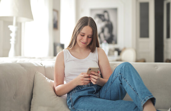 Young woman smiling while using a smartphone on the couch
