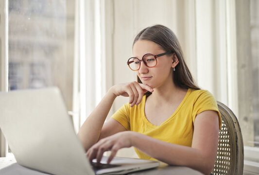 Thoughtful young woman in glasses using laptop