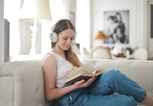 Teenage girl with headphones reads a book on sofa
