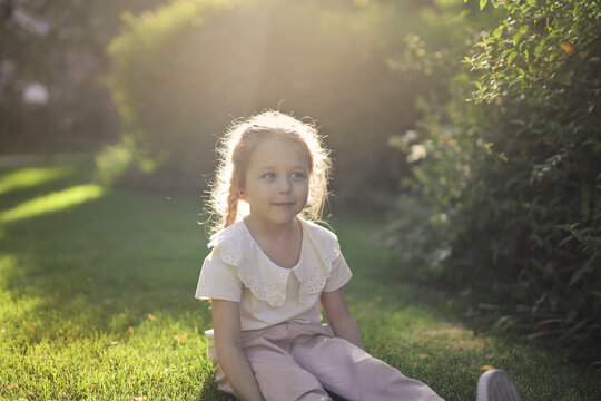 Young girl with braided hair sits on grass at sunset