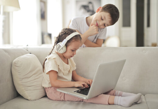 Smiling boy watching his sister use a laptop at home
