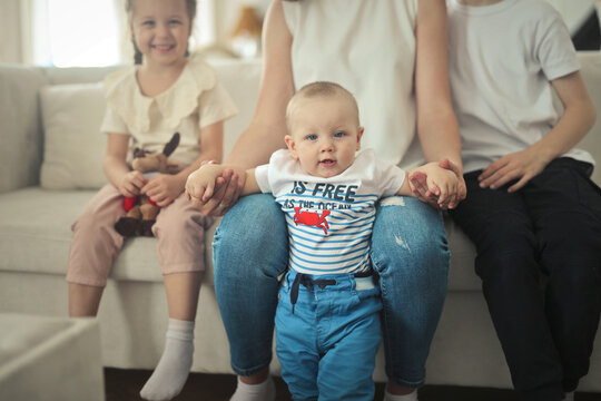 Baby boy stands on moms lap with siblings