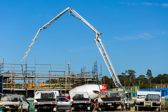 tradies utes parked beside worksite with concrete pump machine towering over scaffolding