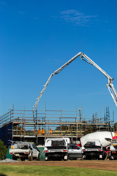 tradies utes parked beside worksite with concrete pump machine towering over scaffolding