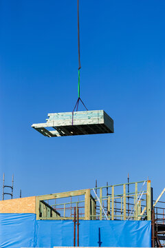 crane at worksite lifting pile of wooden frames for building in sky above construction site