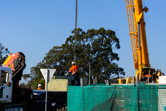 person guiding crane at worksite lifting pile of wooden framework for building