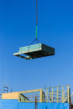 crane at worksite lifting pile of wooden frames for building in sky above construction site