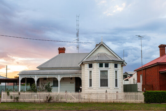 Old weatherboard building with verandah and tin roof behind white picket fence