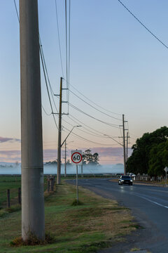 car at dawn traveling road beside farm paddocks with powerlines crossing overhead