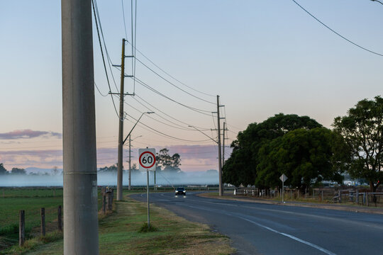 car at dawn traveling road beside farm paddocks with powerlines crossing overhead