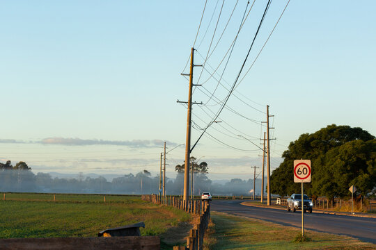 sunrise light on cars traveling road beside farm paddocks with powerlines crossing overhead