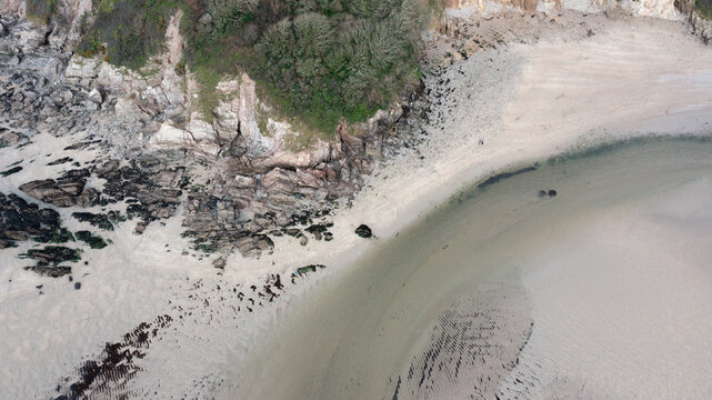 Aerial view of the sandy shores and rugged rocky cliffs at Mothecombe Beach with the river Erme flowing into the sea and people on the sand at Mothecombe, Devon, United Kingdom.