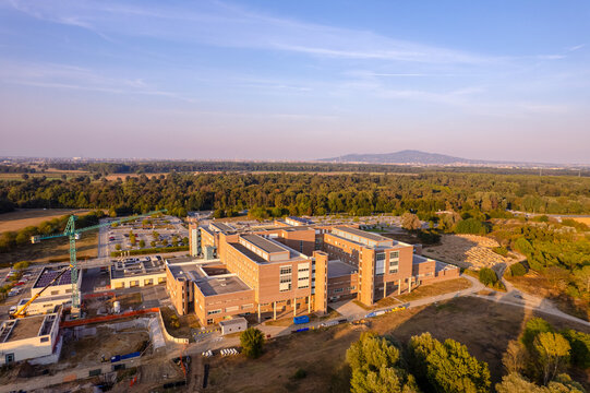 Aerial view of the Oncological Institute Candiolo medical complex featuring modern brick buildings, a construction crane, and parking areas near a forest Candiolo, Piemonte, Italy.
