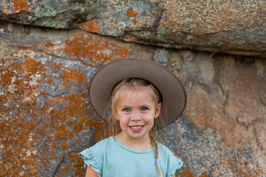 Little Australian girl against rock backdrop wearing Akubra hat outdoors