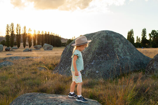 Australian child playing on rocks in grassy paddock at sunset enjoying the summer evening