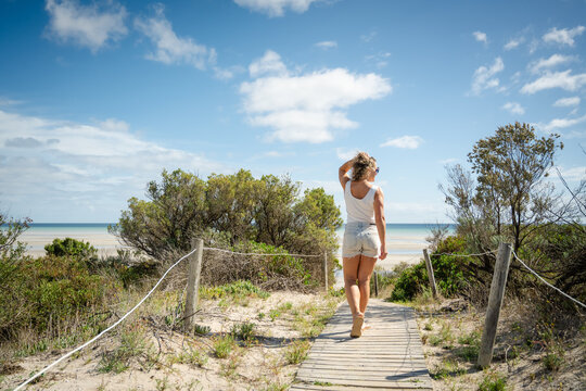 woman walking on slat wood beach path with beach in background