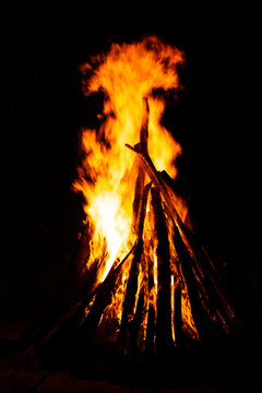 Bonfire with forked flames rising above teepee logs at night
