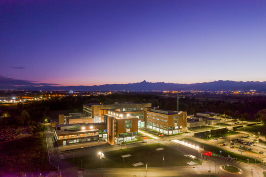 Aerial view of the Oncological Institute Candiolo illuminated at dusk with the Alps mountain range in the background under a purple twilight sky Candiolo, Piemonte, Italy.