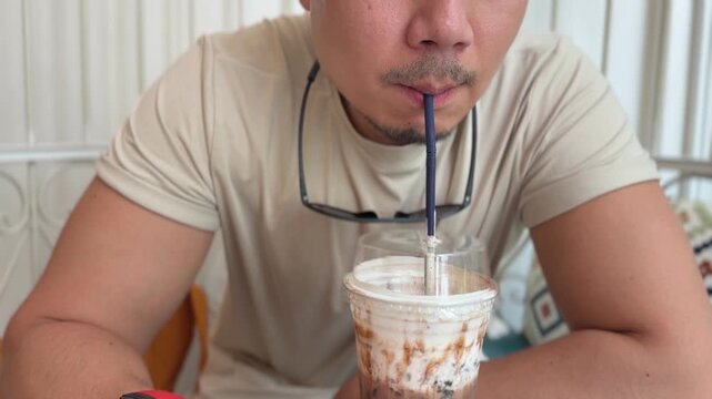 Man enjoys a refreshing iced coffee beverage through a straw in a casual cafe setting.