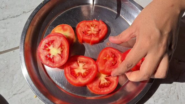 Close-up of hands slicing fresh red tomatoes on a steel plate in sunlight
