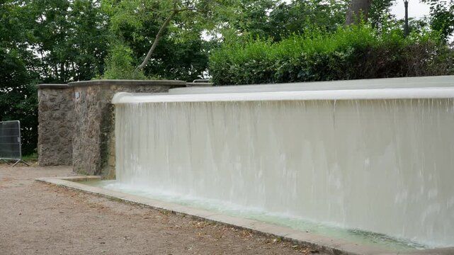 Artificial cascade fountain pours water inside Montmartre park garden in Paris France. Urban landscape architecture design features public park infrastructure for summer tourism travel trip.