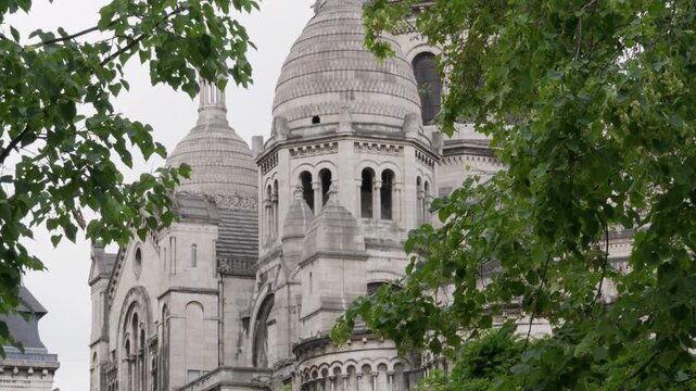 Sacre Coeur basilica church dome stands behind green tree branches in Paris France. Roman Catholic cathedral architecture represents historic European landmark tourism travel holiday trip.