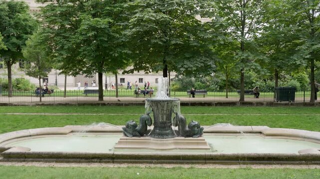 Square Berlin garden fountain splashes water inside a public park in Paris France. Classic municipal landscape architecture features stone dolphin sculptures for city recreation leisure.