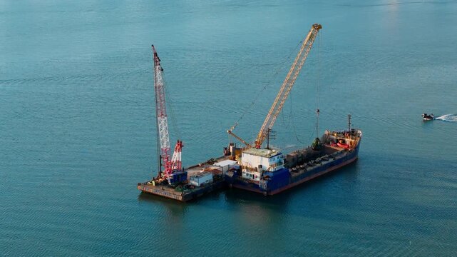 Industrial dredging setup in calm sea water with crane barge and support vessel. Aerial view of marine maintenance and waterway management