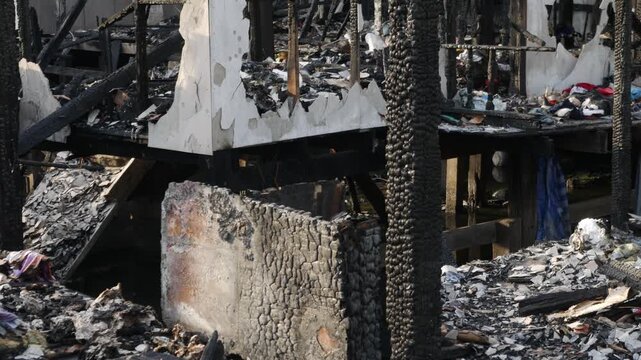 Fire disaster aftermath exterior view of burned destroyed residential house with charred wooden columns collapsed structure and debris