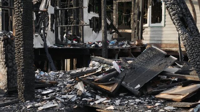 Fire disaster aftermath exterior view of burned destroyed residential house with charred wooden columns collapsed structure and debris
